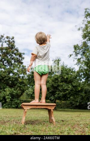 Ansicht von hinten von einem kleinen Kind Junge stehend auf Schemel erreichen in den Himmel. Stockfoto