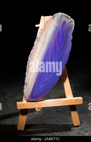 Studio shot eines länglichen, dünnen und poliert Achat Scheibe in der vorderen Beleuchtung mit blauen und weißen Streifen Diagonal stehend auf eine Miniatur Staffelei. Stockfoto