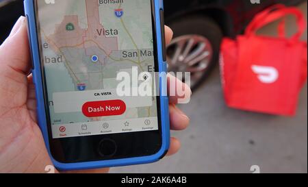 In der Nähe der Person, die die Anmeldung bei der DoorDash dasher App zu beginnen. Im Hintergrund sehen wir ein Auto und ein DoorDah heiße Tasche, alle bereit zu gehen. Stockfoto