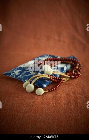 Buddhistische Juzu Perlen liegen oben auf einem silk Perle Beutel. Auf einem Tuch Hintergrund einer Farbe ähnlich gebrannte Sienna fotografiert. Stockfoto