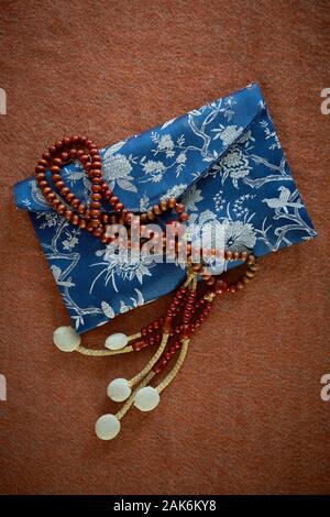 Buddhistische Juzu Perlen liegen oben auf einem silk Perle Beutel. Auf einem Tuch Hintergrund einer Farbe ähnlich gebrannte Sienna fotografiert. Stockfoto