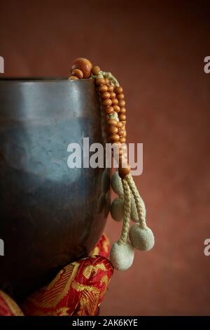 Buddhistische Juzu Gebetsperlen hängt über der Seite einer Glocke auf Lotus Kissen. Auf einem Tuch Hintergrund ähnlich wie die Farbe der gebrannte Sienna fotografiert. Stockfoto