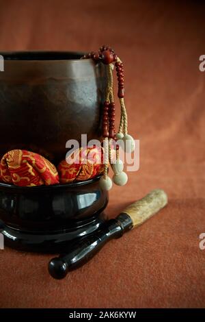 Buddhistische Juzu Gebetsperlen hängt über der Seite einer Glocke auf Lotus Kissen. Auf einem Tuch Hintergrund ähnlich wie die Farbe der gebrannte Sienna fotografiert. Stockfoto