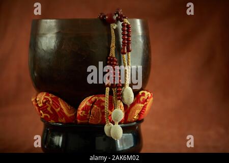 Buddhistische Juzu Gebetsperlen hängt über der Seite einer Glocke auf Lotus Kissen. Auf einem Tuch Hintergrund ähnlich wie die Farbe der gebrannte Sienna fotografiert. Stockfoto