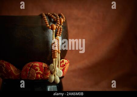 Buddhistische Juzu Gebetsperlen hängt über der Seite einer Glocke auf Lotus Kissen. Auf einem Tuch Hintergrund ähnlich wie die Farbe der gebrannte Sienna fotografiert. Stockfoto