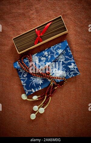 Buddhistische Juzu Perlen liegen auf einer Seide bead Tasche, neben einer Box von Räucherstäbchen. Schuß auf einem Tuch Hintergrund einer Farbe ähnlich gebrannte Sienna. Stockfoto
