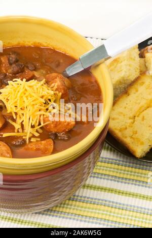 Hausgemachte Chili mit schwarzen Bohnen und Polska Wurst mit Cheddar Käse auf der Oberseite. Mit Gelben cornbread auf der Seite gedient. Stockfoto