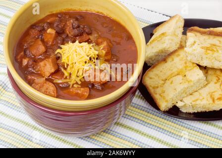 Hausgemachte Chili mit schwarzen Bohnen und Polska Wurst mit Cheddar Käse auf der Oberseite. Mit Gelben cornbread auf der Seite gedient. Stockfoto