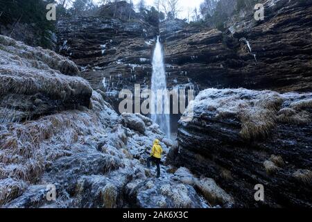 Frau, die unter einem halbgefrorenen Pericnik Wasserfal mit Eiszapfen im Rücken im atemberaubenden Vrata-Tal, Julische alpen, Slowenien steht Stockfoto