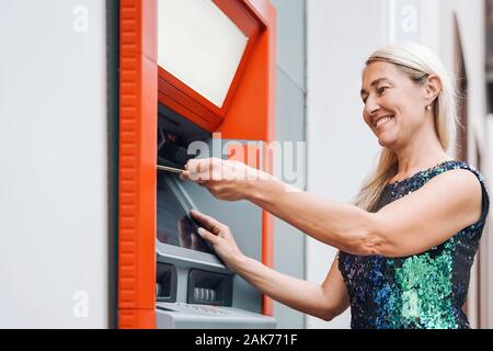 Gerne reife Frau Geld von der Bank Geldautomaten abheben mit der ec-Karte - Ältere Frauen tun, Bezahlung mit Kreditkarte in ATM Stockfoto