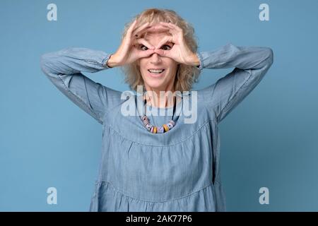 Pretty Woman holding Finger in die Nähe von Augen wie eine Brille. Maske wie super Held oder Eule auf blauem Hintergrund isoliert. Ich echte Gläser Konzept Stockfoto