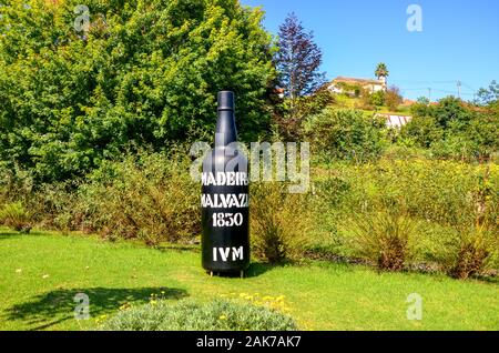 Santana, Madeira, Portugal - Sep 24, 2019: Riesige Flasche Wein Madeira Wein als Exponat auf Madeira Themenpark. Große schwarze Flasche Wein im Freien umgeben von grünen Bäumen. Stockfoto