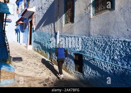 Ein Mädchen mit Geflecht und ihrem Schatten in der sonnigen Straße der Medina von Chefchaouen (auch bekannt als Chaouen), Marokko Stockfoto