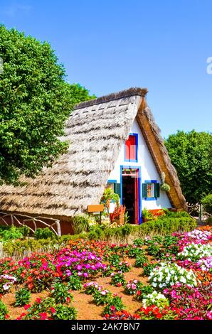 Schönes traditionelles Haus in Santana, Madeira, Portugal. Holz-, dreieckigen Häuser bilden einen Bestandteil des Portugiesischen Erbe. Vorderer Garten mit schönen bunten Blumen. Touristische Attraktion. Stockfoto