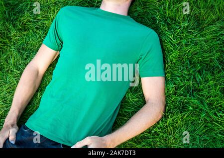 Unerkennbarer junger Mann in grünem T-Shirt mit Copy-Platz im Freien in einem Flecken üppigen Grases Stockfoto