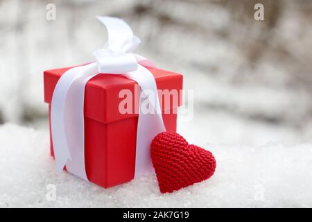 Geschenkbox mit Rot gestrickt Herz auf dem Schnee im Winter Park, selektiven Fokus. Romantisch in Valentinstag, Konzept der Liebe und Geburtstag. Stockfoto