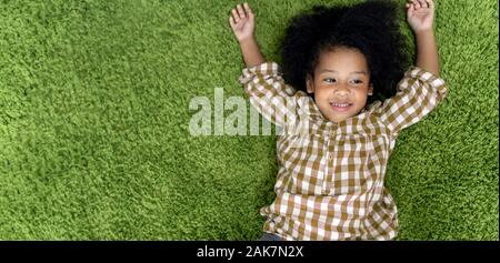 Glückliche Kinder kleine Mädchen lächelnd und Festlegung auf grünem Teppichboden im Wohnzimmer zu Hause. Stockfoto