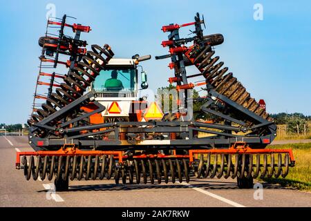 Ist ein Betriebsinhaber zu fahren gesehen ein großer Industrieller Traktor von hinten, mit der Ausdehnung der rotierenden Bodenbearbeitung und Anhang für die Bewirtschaftung von Ackerland Pflug Stockfoto