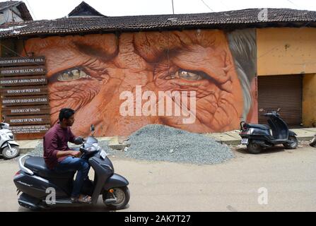 Ein indischer Mann, der durch ein buntes Wandgemälde in Fort Kochi, Indien hetzt. Stockfoto