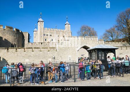 Schule Kinder queuing außerhalb der Mauern von Henry III watergate Eingang mit der berühmten Weißen Turm im Hintergrund, der Tower von London, England, Großbritannien Stockfoto