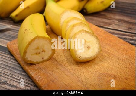 Eine reife, gelbe Banane schneiden in mehrere Stücke auf einem Holzbrett auf einer hölzernen Hintergrund. Nahaufnahme Stockfoto