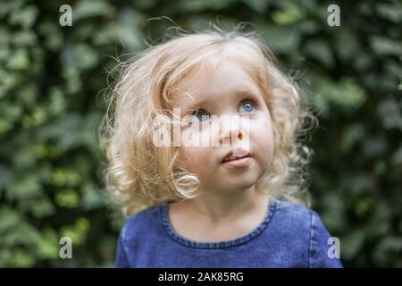 Porträt einer wenig schönen europäischen Mädchen mit Lockigen, blonden Haaren und blauen Augen von 3 bis 4 Jahren in einem klassischen Blau Kleid, trendige Farbe 2020 Stockfoto