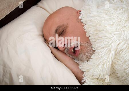 Grauhaariger Mann schlafend auf dem Bett unter ein flauschiges Plaid. Stockfoto