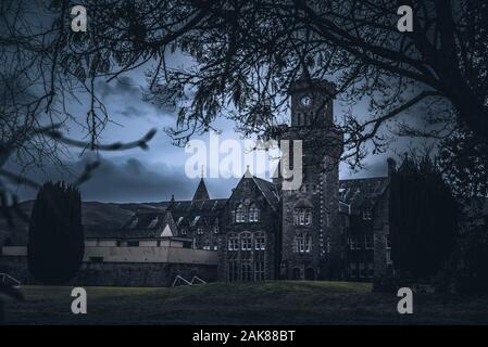FORT AUGUSTUS, Schottland, 17. Dezember 2018: Die Abtei Highland Club Clock Tower, voller Schimmel und Flechten in seinen Steinmauern, unter starkem cloudscape Stockfoto