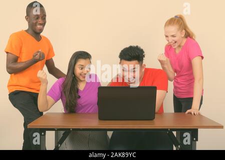 Studio shot von Happy vielfältige Gruppe von multi-ethnische Freunde lächelnd, während sie motiviert und mit Laptop auf hölzernen Tisch Stockfoto