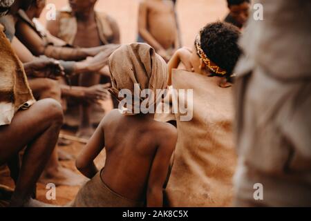 Afrikanische Kind von hinten in die soziale Gruppe der Menschen in traditionellen Dorf sitzen Stockfoto