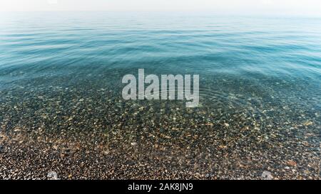 Die glatte Oberfläche des Meeres bei gutem Wetter. Reines klares blaues Wasser. Meer Kiesel sind sichtbar durch die Wassersäule. Stockfoto