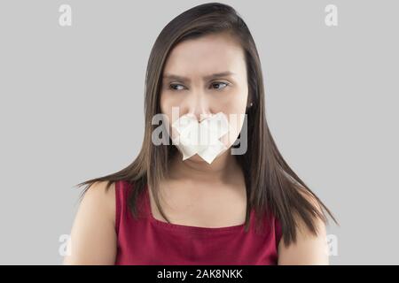 Asiatische Frauen in roten Kleidern mit Abdeckband den Mund zu schließen, weil sie nicht auf einem grauen Hintergrund zu kommentieren, Thai Frauen in mit Klebstoff Stockfoto