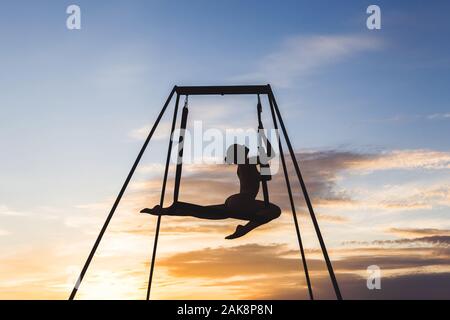 Schöne Mädchen üben Fliegen - Yoga Posen in einer Hängematte im Freien bei Sonnenuntergang. Sport Konzept. Abstrakte und Konzept weiblichen Sport Foto. Akrobatische Gymnastik dar. Stockfoto