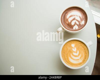 Zwei Tassen Cappuccino und heißer Kakao mit schönen Latte Art auf einem grauen hölzernen Tisch in einem Cafe mit Copyspace. Stockfoto