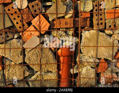 Eine handgemachte Gabione Wand in einem Vorort Garten verwendet, gebrochene Ziegel und Beton und Rohre von der Seite Stockfoto