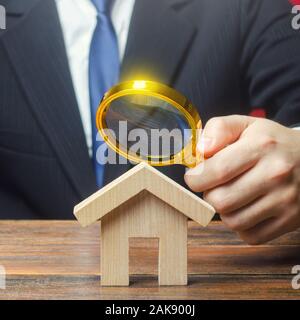 Ein Mann studiert ein Haus durch ein Vergrößerungsglas. Verkehrswert der Immobilien. Immobilienbewertung. Rechtliche beschäftigen. Standards und Qualität der Konstruktion Stockfoto