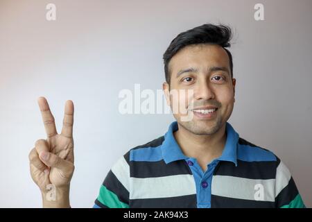 Ein junger Inder zuversichtlich und lächelnd zeigt zwei Sieg Symbol auf weißem Hintergrund mit Kopie Platz für Text isoliert. Stockfoto