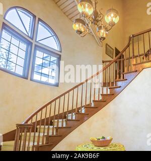 Quadratischen rahmen Spindeltreppe in einem warmen Landhausstil home mit Kronleuchter und einem kleinen Tisch Stockfoto
