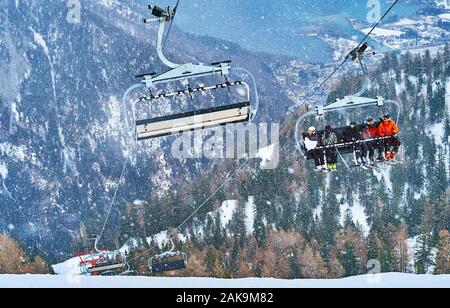 EBENSEE, Österreich - 24. Februar 2019: Der Blick vom Feuerkogel Berghang auf Sesselbahn mit Sportlern, Traunsee und Alpen unter der Schneefall ein Stockfoto