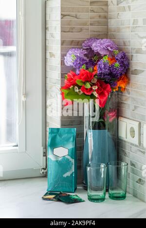 Nahaufnahme der Vase mit Blumen und zwei Gläser auf den weißen Fensterbank. Stockfoto