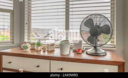 Pano eingetopfte Kakteen und elektrischer Ventilator auf Holzgehäuse gegen Bay Fenster eines Home Stockfoto