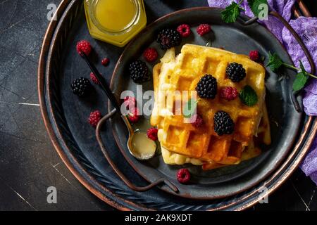 Frühstück. Hausgemachten belgischen Waffeln mit Beeren und Honig auf dunklen Tisch. Ansicht von oben flach. Stockfoto