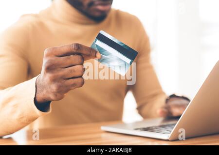 Geld übertragen. Nicht erkennbare afrikanischen Guy holding Kunststoff Kreditkarte und mit Laptop. Platz kopieren Stockfoto