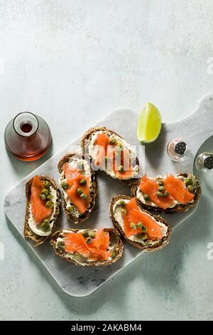 Roggen Brot Sandwiches mit geräuchertem Lachs und Kapern auf einem Marmor- und Sesamöl mit Schichten aus Kalk Stockfoto