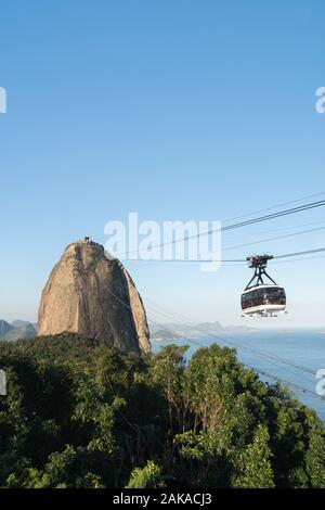 Ein Sugarloaf Mountain Seilbahn in der Luft über tropische Bäume in Rio de Janeiro an einem sonnigen Abend. Stockfoto