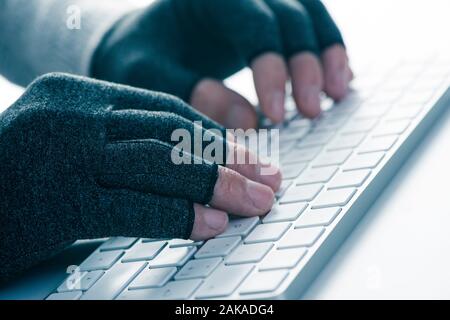 Nahaufnahme von einem kaukasischen Mann tragen ein Paar Handschuhe während der Kompression ist die Eingabe über die Tastatur des Computers Stockfoto