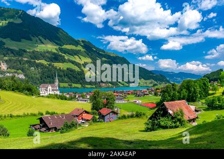 Katholische Kirche, traditionelle und moderne Häuser an der See im Schweizer Dorf Lungern Lungernsee im sonnigen Sommertag, Obwalden, Schweiz Stockfoto