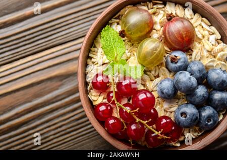 Flach auf Hafer in Ton Schüssel mit Beeren auf hölzernen Tisch Stockfoto