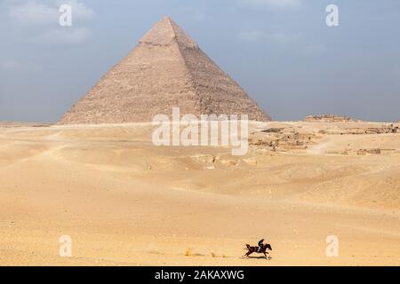 Ein Mann reitet auf einem Pferd durch die Wüste Sand auf Gizeh Plateau in der Nähe der Pyramiden von Ägypten Stockfoto