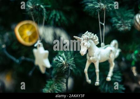 White unicorn als Christbaumschmuck hängen am Weihnachtsbaum in der Gesellschaft von Christbaumkugeln, eine orange Patch und weißen Sternen. Stockfoto